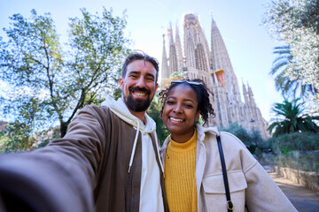 Multiracial young couple taking a selfie in front of the sagrada familia, enjoying their vacation...