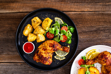 Oven roasted chicken thigh with potatoes and fresh salad on wooden table