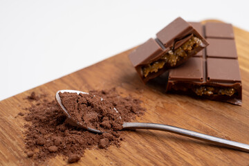 Spoon with cocoa powder and delicious chocolate with filling on table, top view. Milk, dark chocolate bar
