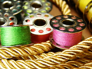 Kolorowe nici na szpulkach widoczne na tle złotego, grubego sznurka