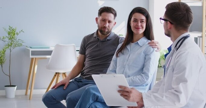 Family couple planning IVF treatment and getting health checkup at clinic. Happy young man and woman having appointment with doctor who shows clipboard and talks about medical exam results