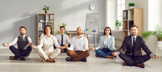 Peaceful young business people meditating and having a rest in office sitting on floor in Lotus...