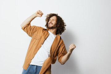 A joyful young man with curly hair celebrating success in a casual outfit, showcasing happiness and...