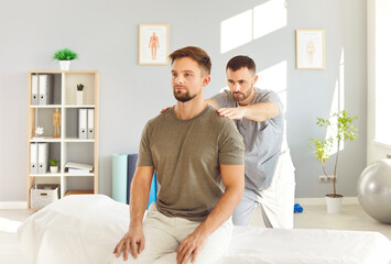 Obraz premium Young doctor osteopath or physiotherapist helping young male patient sitting on the couch in modern rehab clinic with healing back pain. Physiotherapy and physical rehabilitation concept.