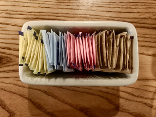 All The Sugar And Sugar Alternative Packets In A Ceramic Dish On A Table