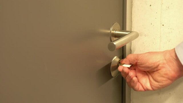 Hand is inserting the modern security key into the door lock of an apartment, unlocking it, and opens the door. 