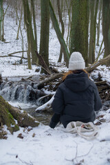 girl sits in the snow near a small mountain waterfall in Bratislava