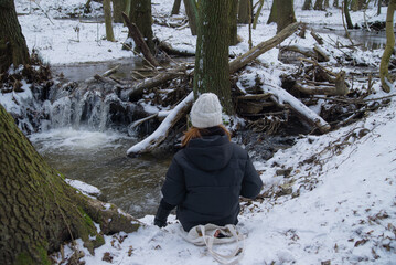 girl sits in the snow near a small mountain waterfall in Bratislava