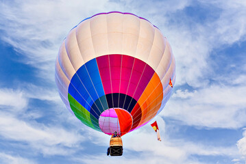 Colorful hot air balloon flying over blue sky with white clouds	