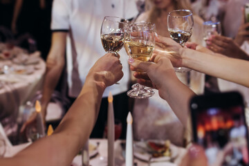 Group of guests celebrate and raise glasses, toasting and cheering with alcohol glasses with wine and champagne in a restaurant on corporate christmas, birthday party prom event or wedding celebration