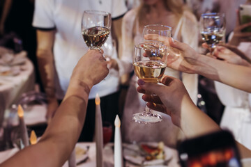Group of guests celebrate and raise glasses, toasting and cheering with alcohol glasses with wine and champagne in a restaurant on corporate christmas, birthday party prom event or wedding celebration