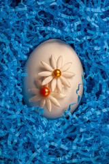 One egg in blue straw and prepared for the Easter holiday.  Egg is decorated with  two handmade  flowers.