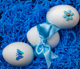 three eggs in blue straw prepared for the Easter holiday. Each egg is decorated with colorful beads, as well as butterflies and stars made of fabric.   some eggs are adorned with blue ribbon