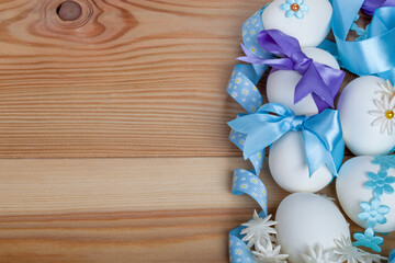 Several eggs are on a wooden table decorated with colorful beads, fabric butterflies, and stars for Easter. Some are adorned with blue ribbons.This festive scene is perfect for an Easter greeting card