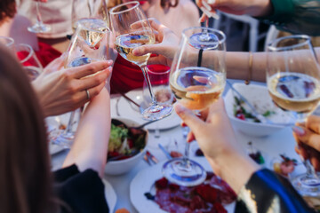 Group of guests celebrate and raise glasses, toasting and cheering with alcohol glasses with wine and champagne in a restaurant on corporate christmas, birthday party prom event or wedding celebration