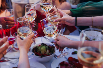 Group of guests celebrate and raise glasses, toasting and cheering with alcohol glasses with wine and champagne in a restaurant on corporate christmas, birthday party prom event or wedding celebration