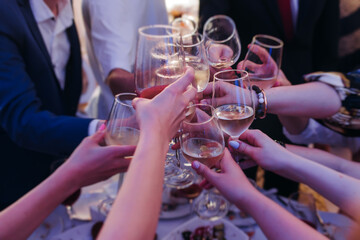 Group of guests celebrate and raise glasses, toasting and cheering with alcohol glasses with wine and champagne in a restaurant on corporate christmas, birthday party prom event or wedding celebration