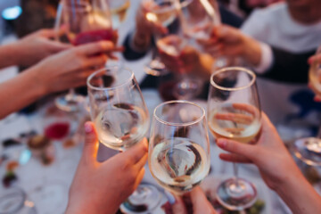 Group of guests celebrate and raise glasses, toasting and cheering with alcohol glasses with wine and champagne in a restaurant on corporate christmas, birthday party prom event or wedding celebration