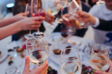 Group of guests celebrate and raise glasses, toasting and cheering with alcohol glasses with wine and champagne in a restaurant on corporate christmas, birthday party prom event or wedding celebration