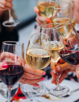 Group of guests celebrate and raise glasses, toasting and cheering with alcohol glasses with wine and champagne in a restaurant on corporate christmas, birthday party prom event or wedding celebration