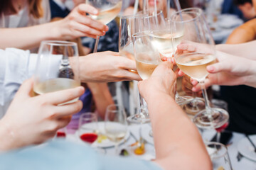 Group of guests celebrate and raise glasses, toasting and cheering with alcohol glasses with wine and champagne in a restaurant on corporate christmas, birthday party prom event or wedding celebration