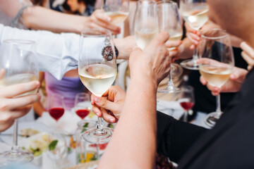 Group of guests celebrate and raise glasses, toasting and cheering with alcohol glasses with wine and champagne in a restaurant on corporate christmas, birthday party prom event or wedding celebration
