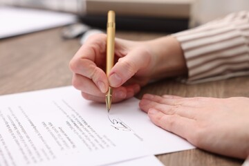 Woman putting signature on document at table, closeup