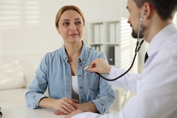 Cardiologist with stethoscope listening patient's heartbeat at desk in clinic
