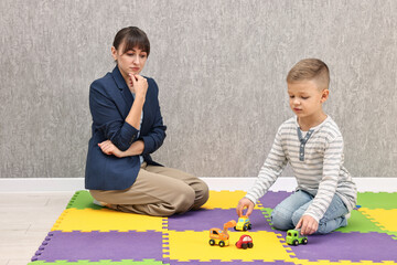 Naklejka premium Psychologist observing little boy playing in autism treatment center