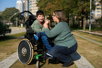 Mother holding hands with son with disability in wheelchair at park
