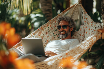 Male businessman in hammock working remotely. Man with laptop resting in hammock on beach, freelance worker using computer in tropical resort