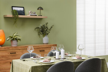 Stylish table setting with olive tablecloth, glasses and candles in dining room