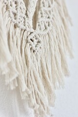 closeup of a handmade macrame wall hanging woven of natural light beige cord on a white background