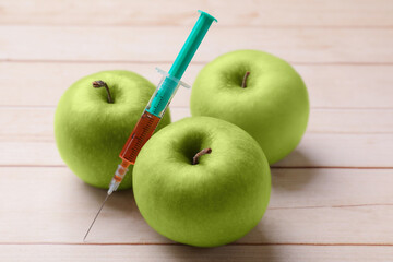 GMO concept. Fresh apples and syringe on wooden table, closeup