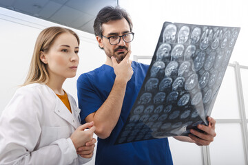 Doctor with MRI of patient head in hands is standing in hospital with male radiologic technologist and at looking in results of tests. Examination of human head