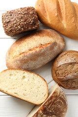 Whole and cut bread loafs on white wooden table, flat lay