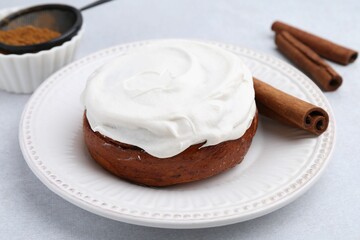 Tasty cinnamon roll with cream and spices on light table, closeup