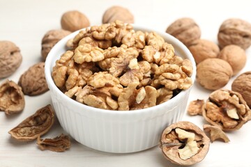 Peeled walnuts in bowl and whole ones on light table, closeup
