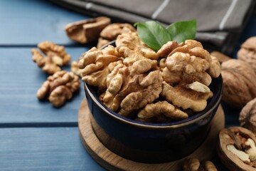 Fresh walnuts and green leaves in bowl on blue wooden table, closeup. Space for text