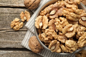 Shelled walnuts in bowl and whole ones on wooden table, flat lay