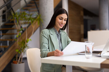 Professional Latina woman analyzing data on a laptop in a bright office