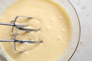 Making dough in bowl with hand mixer at grey table, top view