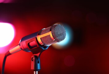 Obraz premium Microphone on stand against red background with blurred lights. Bokeh effect