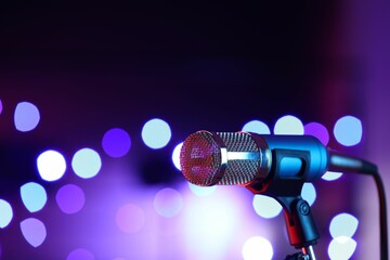 Obraz premium Microphone on stand against color background with blurred lights, space for text. Bokeh effect