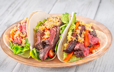 Three carne asada tacos filled with steak, grilled peppers, lettuce, and cheese
