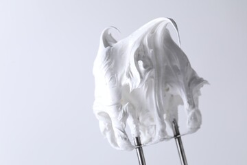 Whisks with whipped cream on white background, closeup. Space for text