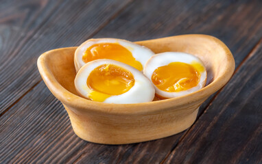 Halved ajitsuke tamago ramen eggs with golden yolks in wooden bowl