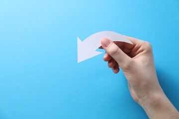 Woman with paper arrow on light blue background, top view. Space for text