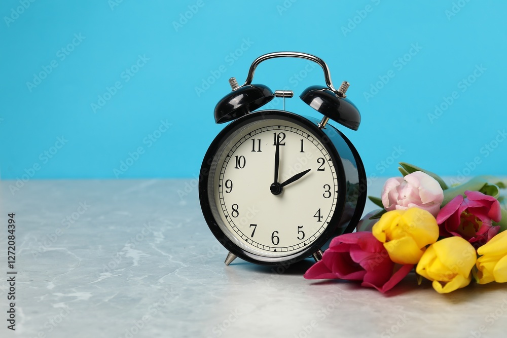 Poster spring time. alarm clock and beautiful tulips on grey marble table against light blue background, sp
