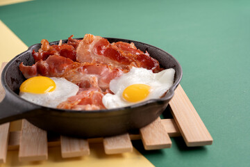 photo Delicious Breakfast Dish with Fried Eggs and Crispy Bacon in Cast Iron Skillet on Wooden Board Perfect for Hearty Morning Meal in Rustic Culinary Style